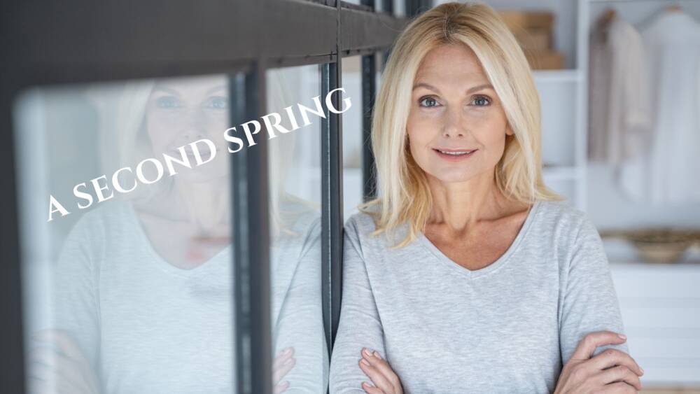 a woman in midlife, smiling with a white shirt and leaning against a window
